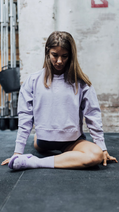 Mujer haciendo estiramientos en el suelo vestida con una sudadera, calcetines y chanclas moradas 